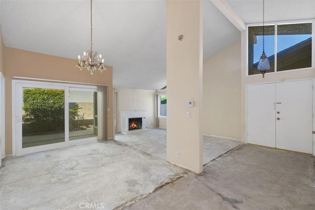 unfurnished living room with high vaulted ceiling, a brick fireplace, a notable chandelier, and concrete floors