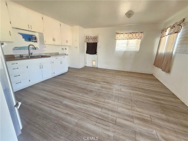 kitchen featuring light countertops, light wood-style floors, freestanding refrigerator, white cabinetry, and a sink