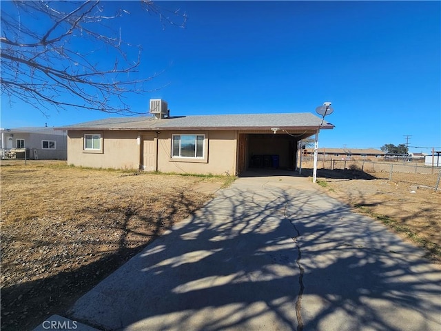 ranch-style home with concrete driveway, central AC unit, fence, and stucco siding