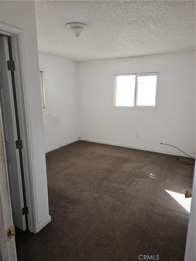 unfurnished room featuring a textured ceiling, dark colored carpet, and baseboards