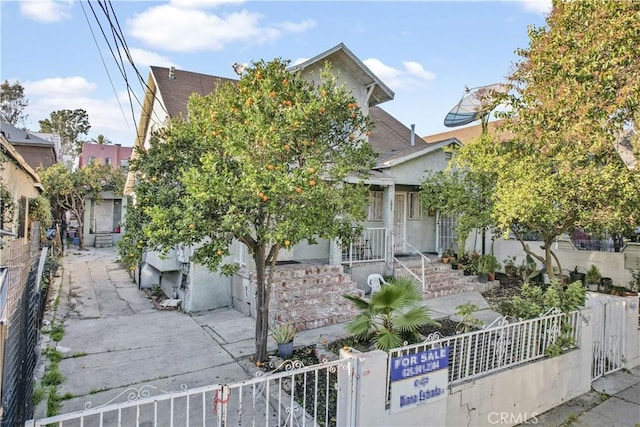 view of property hidden behind natural elements featuring a fenced front yard, a gate, and stucco siding