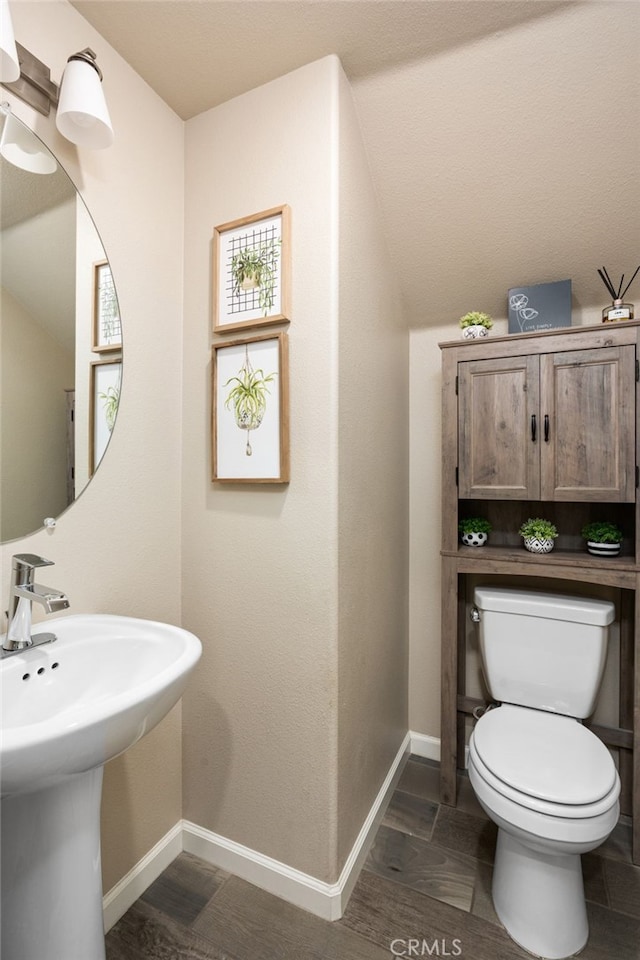 half bath with toilet, a sink, baseboards, and wood finished floors