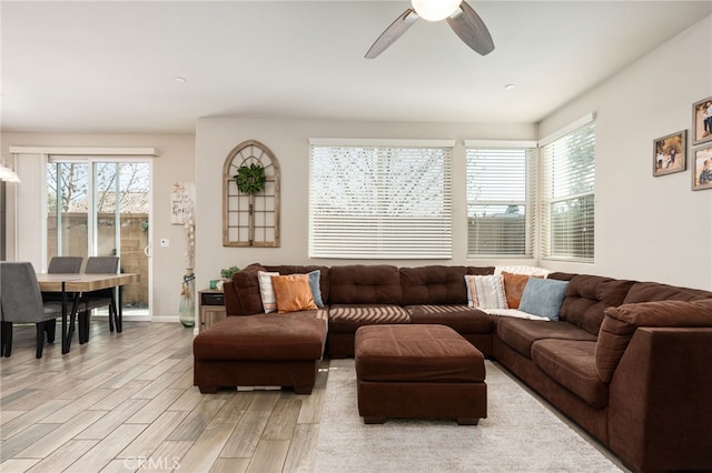 living area featuring a ceiling fan, baseboards, and light wood finished floors