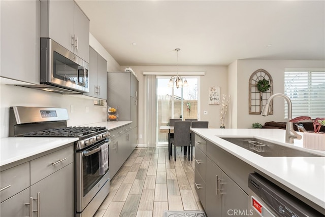 kitchen with decorative light fixtures, stainless steel appliances, light countertops, gray cabinetry, and a sink