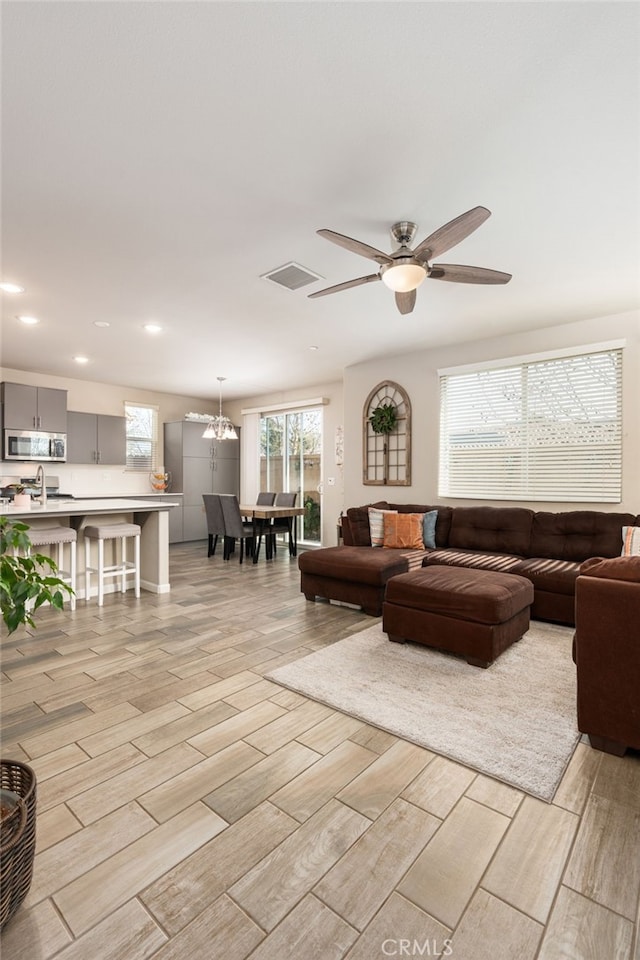 living area with ceiling fan with notable chandelier, wood finish floors, visible vents, and recessed lighting