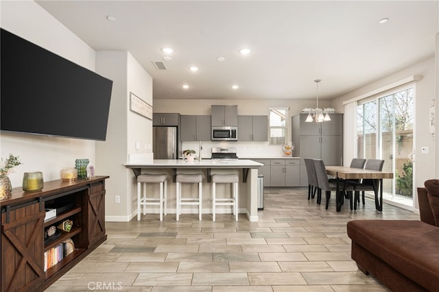 kitchen with a breakfast bar area, a peninsula, light countertops, appliances with stainless steel finishes, and gray cabinets