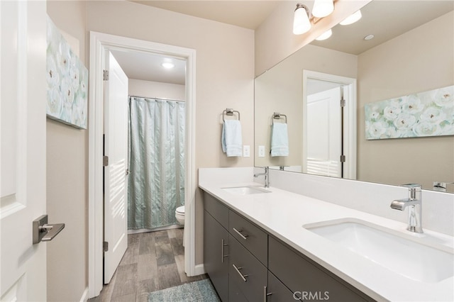 full bath with toilet, double vanity, a sink, and wood finished floors