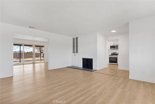 unfurnished living room with a brick fireplace, visible vents, baseboards, and light wood-style floors