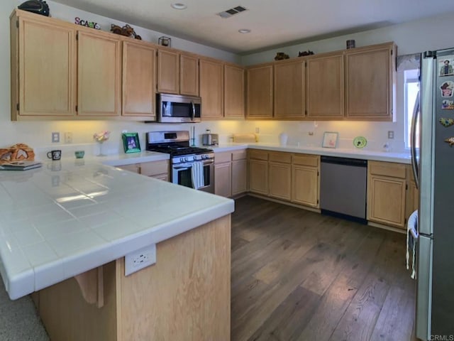 kitchen with light brown cabinets, a peninsula, visible vents, appliances with stainless steel finishes, and dark wood-style floors