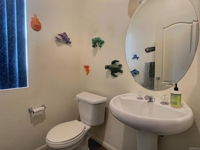 half bathroom with baseboards, a sink, and toilet