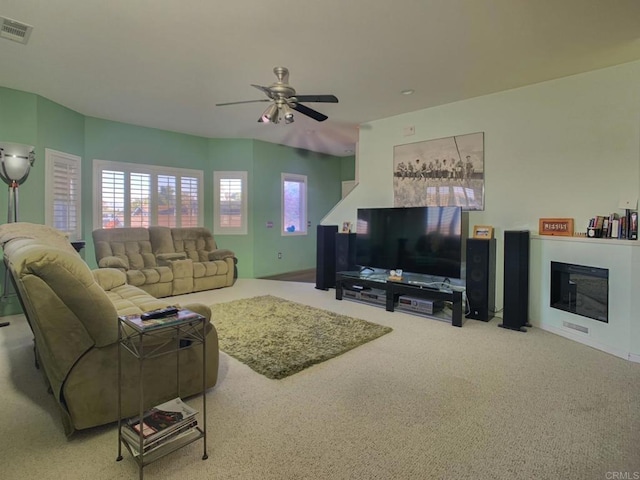 living room featuring carpet, visible vents, a ceiling fan, and a glass covered fireplace