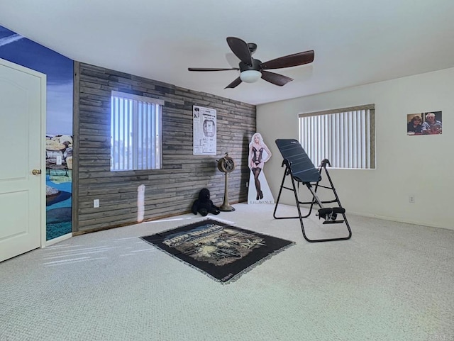 workout room featuring an accent wall, carpet, wooden walls, and a ceiling fan