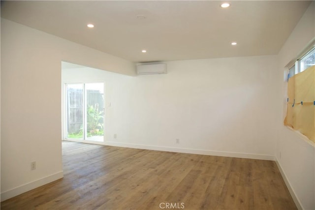 spare room featuring recessed lighting, baseboards, light wood-style floors, and a wall unit AC