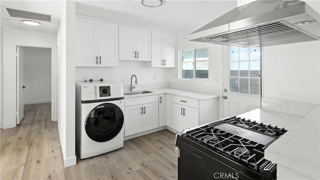 3659 W 110th St, Inglewood, CA 90303 - kitchen with washer / dryer, black range with gas cooktop, wall chimney exhaust hood, light wood-style floors, and white cabinets