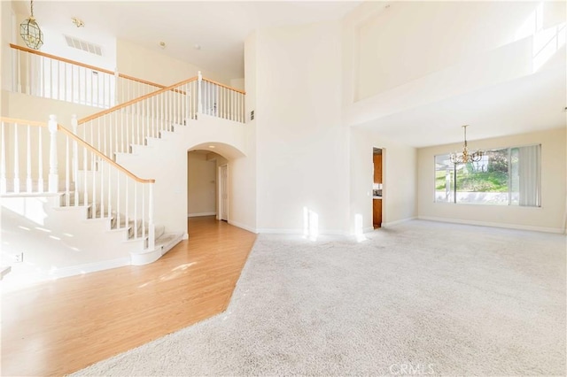 unfurnished living room featuring arched walkways, a notable chandelier, visible vents, stairway, and a towering ceiling