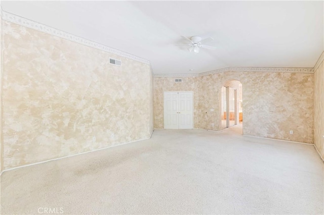 unfurnished room with visible vents, arched walkways, a ceiling fan, crown molding, and carpet flooring