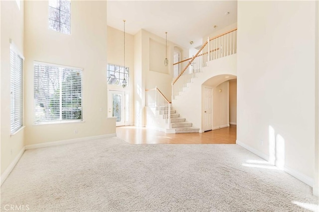 unfurnished living room featuring arched walkways, baseboards, stairs, and light colored carpet