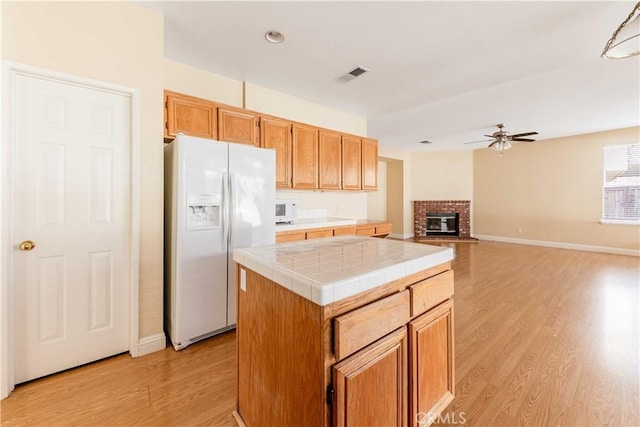 kitchen with a center island, white refrigerator with ice dispenser, tile counters, visible vents, and open floor plan