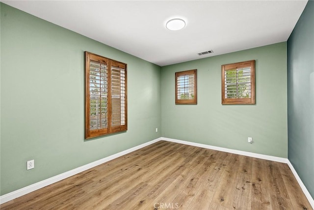 unfurnished room featuring baseboards, visible vents, and wood finished floors