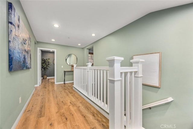 corridor with recessed lighting, wood finished floors, an upstairs landing, and baseboards