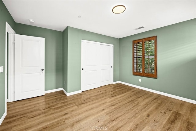 unfurnished bedroom with visible vents, a closet, baseboards, and wood finished floors