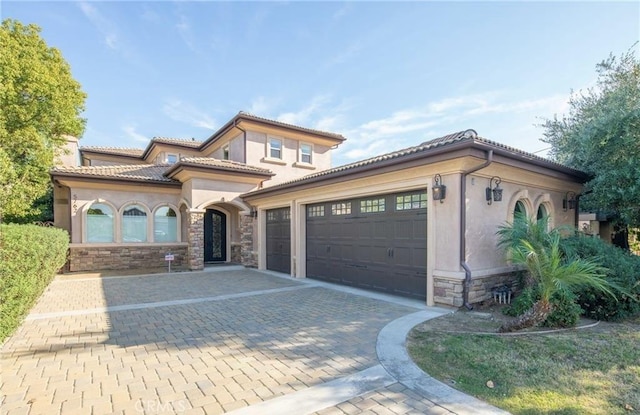 mediterranean / spanish-style house featuring a garage, a tile roof, stone siding, decorative driveway, and stucco siding