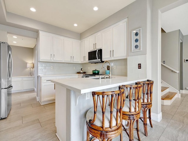 kitchen featuring light countertops, freestanding refrigerator, white cabinetry, a sink, and a peninsula