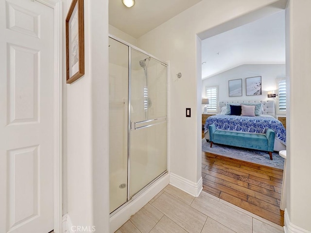 ensuite bathroom with lofted ceiling, connected bathroom, wood finished floors, baseboards, and a shower stall