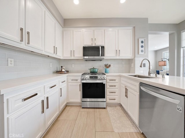 kitchen featuring decorative backsplash, white cabinets, stainless steel appliances, light countertops, and a sink