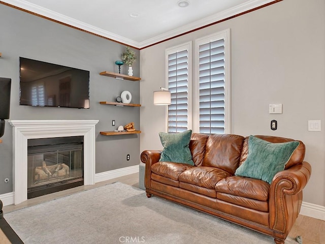 living area featuring light wood-style floors, baseboards, crown molding, and a glass covered fireplace