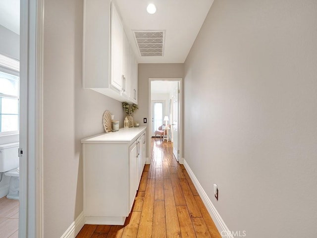 hallway featuring visible vents, plenty of natural light, light wood finished floors, and baseboards