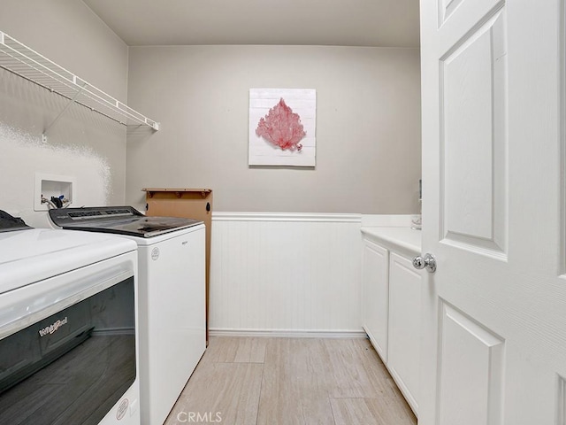 clothes washing area with cabinet space, light wood-style flooring, washer and clothes dryer, and wainscoting