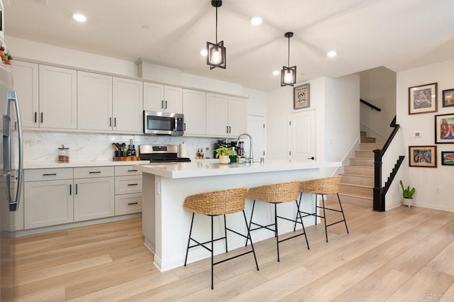 kitchen with hanging light fixtures, a center island with sink, stainless steel appliances, and light countertops