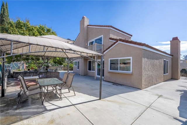 rear view of house with a balcony, a chimney, a tiled roof, a patio area, and stucco siding