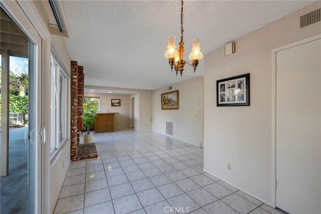 empty room featuring a textured ceiling, light tile patterned floors, visible vents, and a notable chandelier