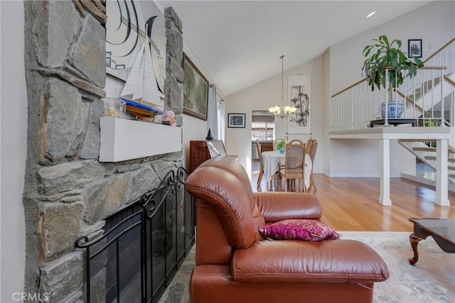 living area featuring high vaulted ceiling, a stone fireplace, a notable chandelier, wood finished floors, and stairway