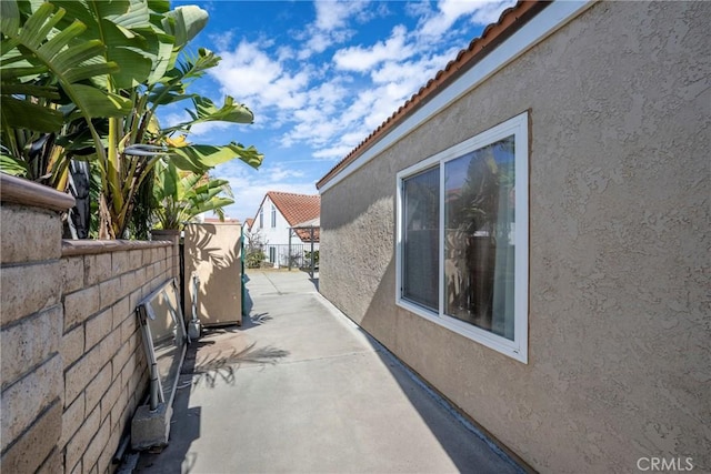 view of side of home with a patio area, a tiled roof, fence, and stucco siding