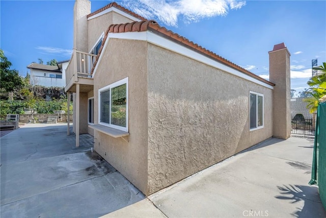 view of property exterior with a tile roof, a patio, a chimney, stucco siding, and fence