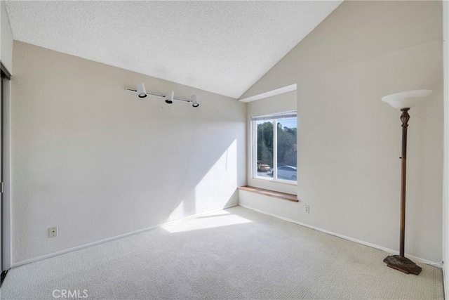 unfurnished room with lofted ceiling, light colored carpet, a textured ceiling, and baseboards