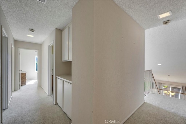 hallway with a textured ceiling, visible vents, and light colored carpet