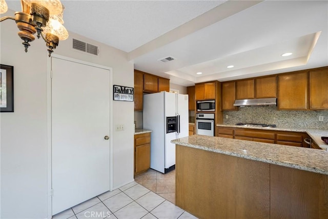 kitchen featuring under cabinet range hood, stainless steel appliances, visible vents, brown cabinetry, and a raised ceiling