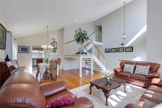 living area with high vaulted ceiling, visible vents, stairway, a chandelier, and light wood-type flooring