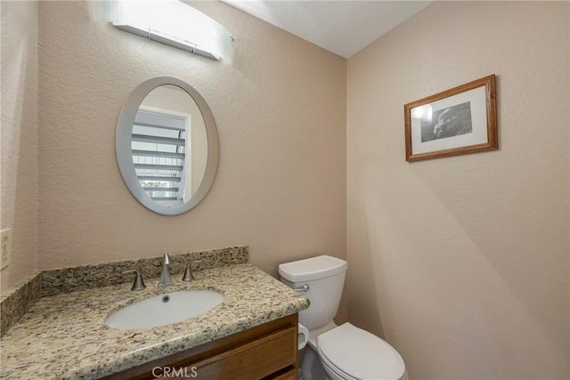 half bath featuring a textured wall, vanity, and toilet