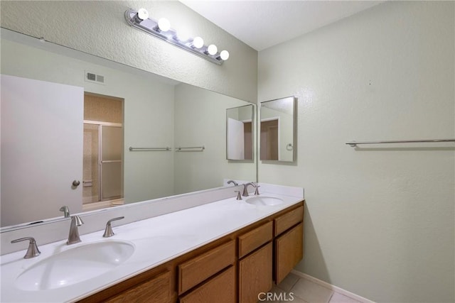 bathroom featuring double vanity, a shower with door, visible vents, and a sink