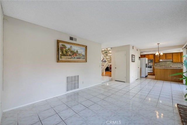 unfurnished room featuring an inviting chandelier, stairs, visible vents, and a textured ceiling