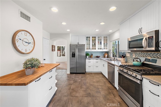 kitchen featuring arched walkways, stainless steel appliances, butcher block counters, visible vents, and decorative backsplash