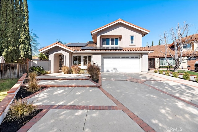 mediterranean / spanish house with concrete driveway, a tiled roof, fence, roof mounted solar panels, and stucco siding