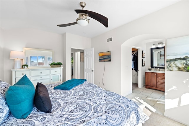 bedroom featuring arched walkways, light tile patterned floors, visible vents, a spacious closet, and ensuite bath