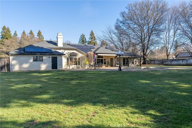 back of house featuring a patio area, roof mounted solar panels, fence, and a yard