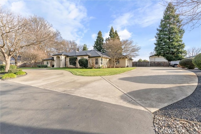 view of front facade with a front yard, stucco siding, driveway, and fence